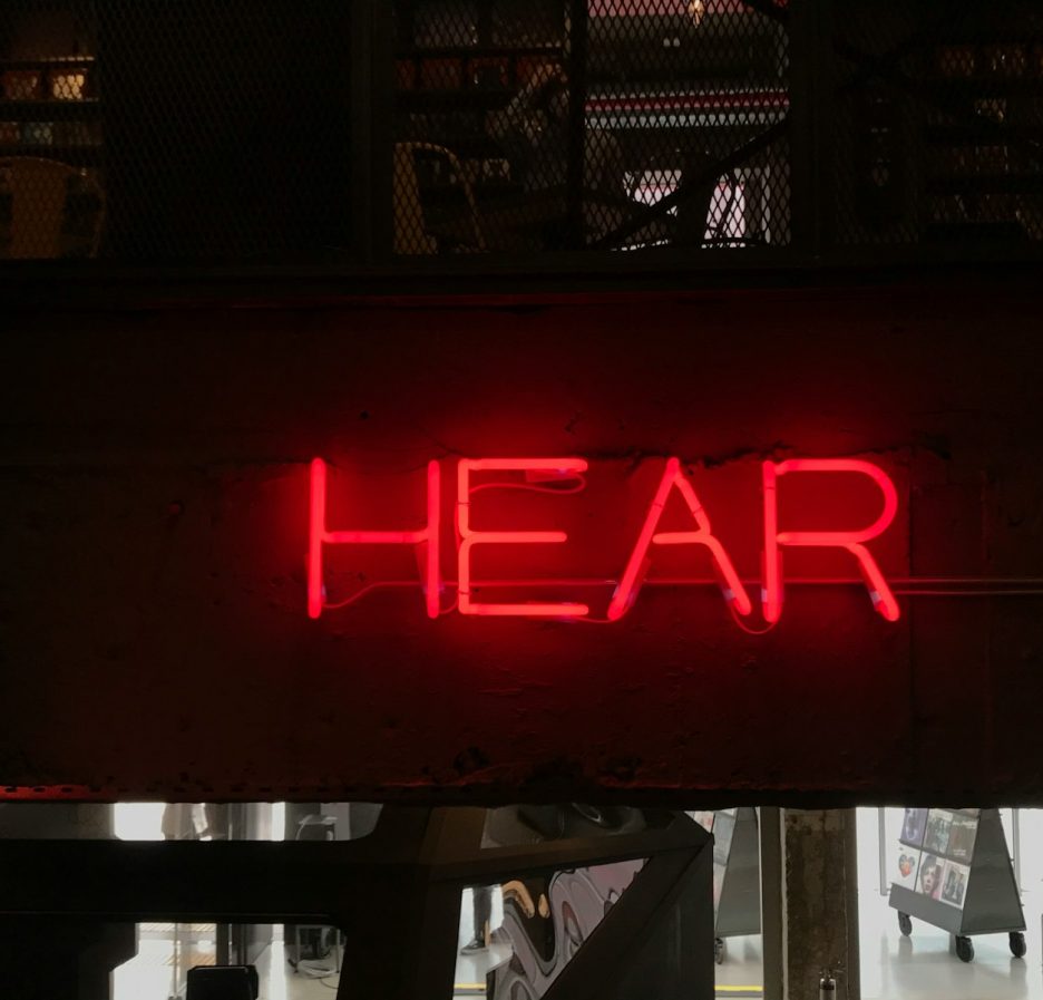 un panneau au néon rouge sur lequel on peut lire « hear » au-dessus d'une porte