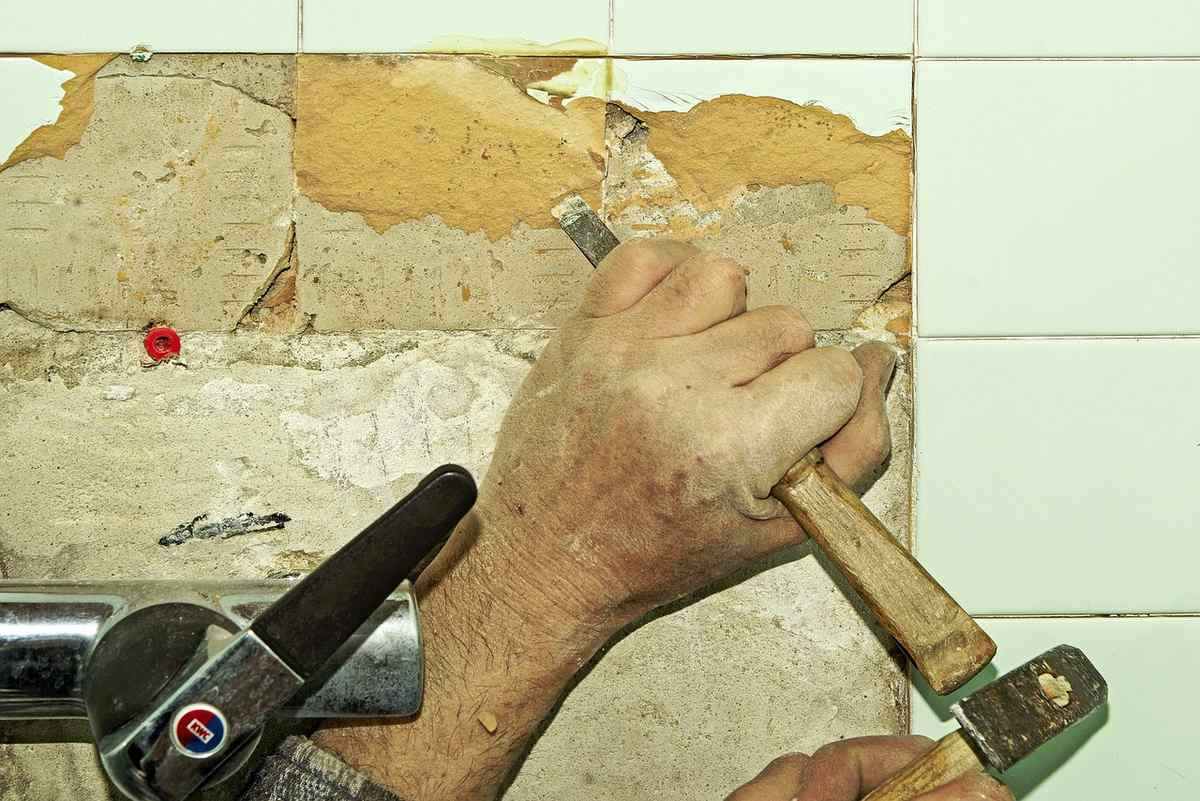 Une main utilise un marteau et un burin pour enlever une tuile Une main utilise un marteau et un burin pour enlever une tuile