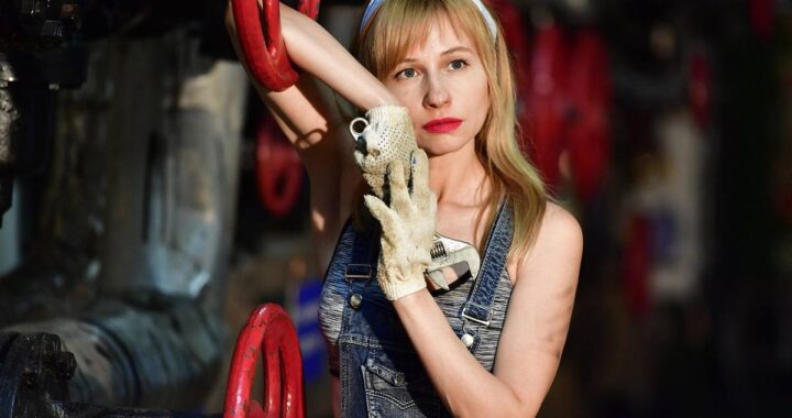 Femme en jean et gants manipulant une manette rouge dans un environnement industriel