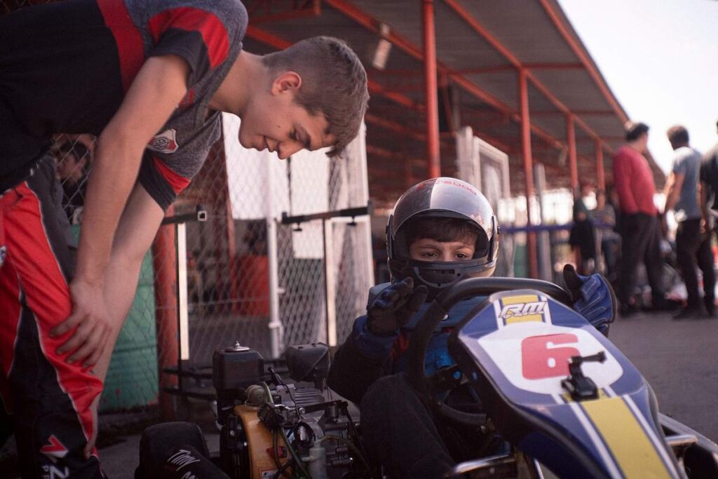 Un jeune pilote de karting reçoit l'aide d'un accompagnateur avant la course