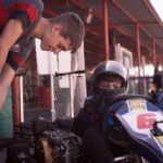 Un jeune pilote de karting reçoit l'aide d'un accompagnateur avant la course
