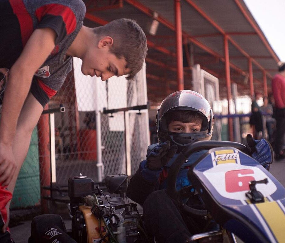 Un jeune pilote de karting reçoit l'aide d'un accompagnateur avant la course